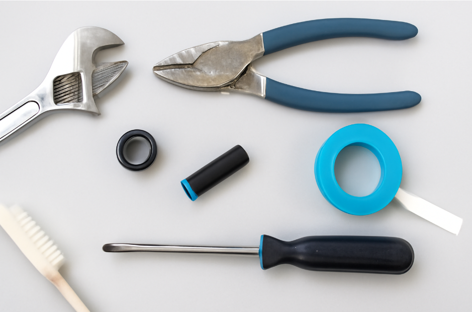 Flat lay of essential plumbing tools including an adjustable wrench, pliers, screwdriver, cleaning brush, and plumber's tape arranged neatly on a gray surface, ready for use in a shower head repair.