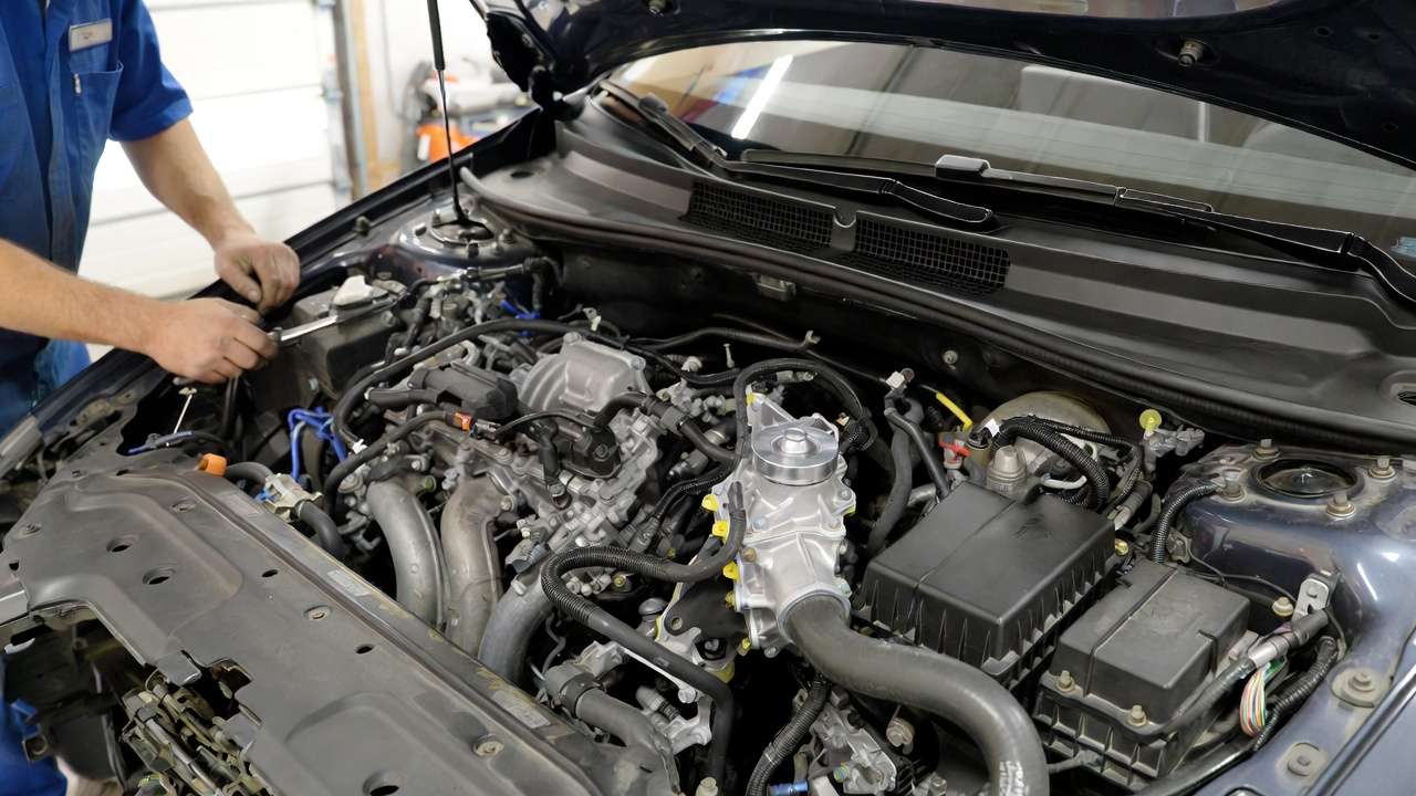 Mechanic upgrading to electric water pump in hybrid engine for better performance.