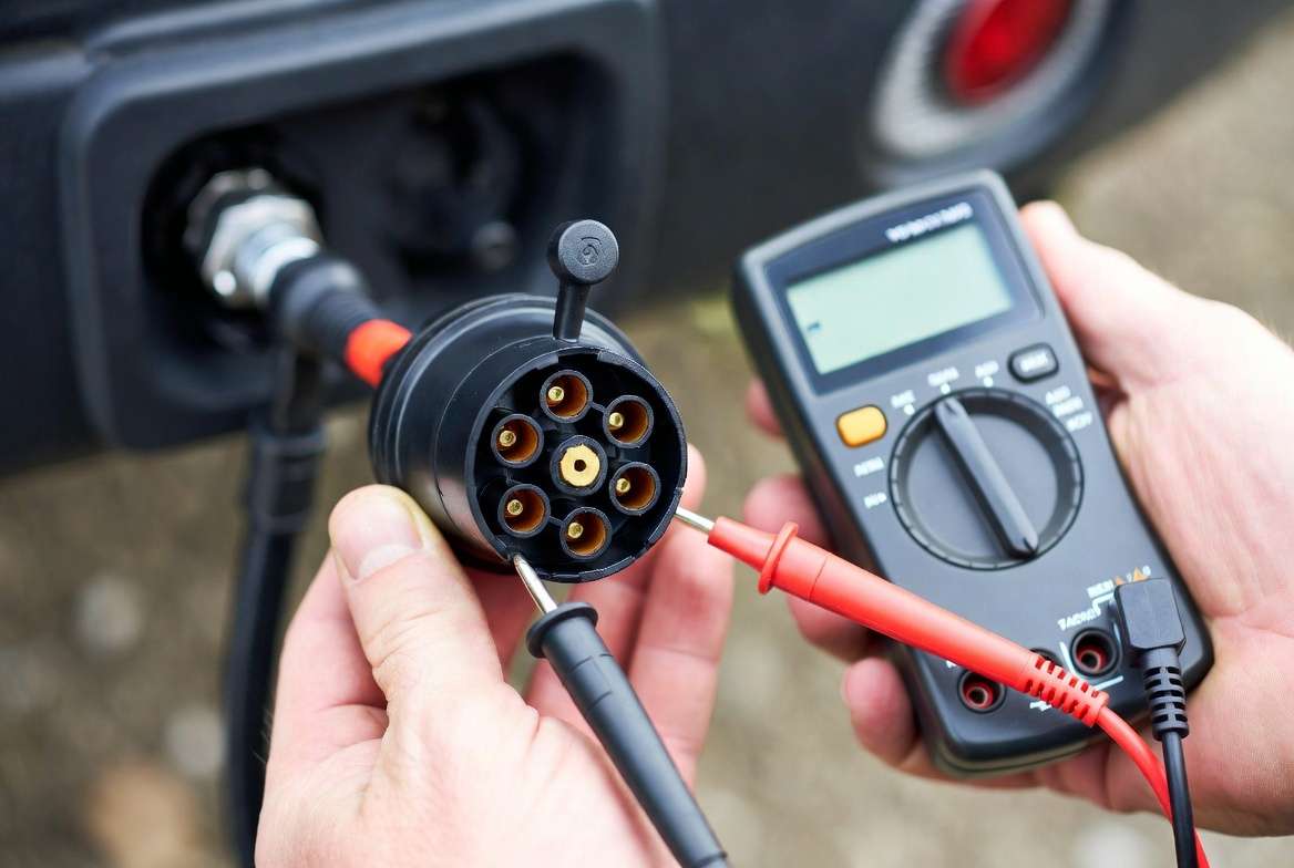 Testing 7-way trailer plug wiring with a multimeter to verify color-coded connections and voltage